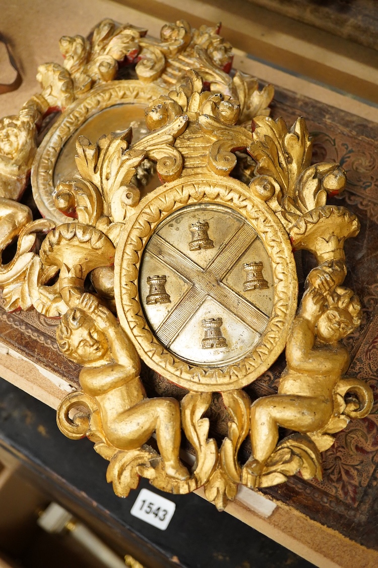 Two gilt metal plaques housed in giltwood ‘cherub’ frames and a heraldic leather folder with watered silk lining, 34 x 27cm
